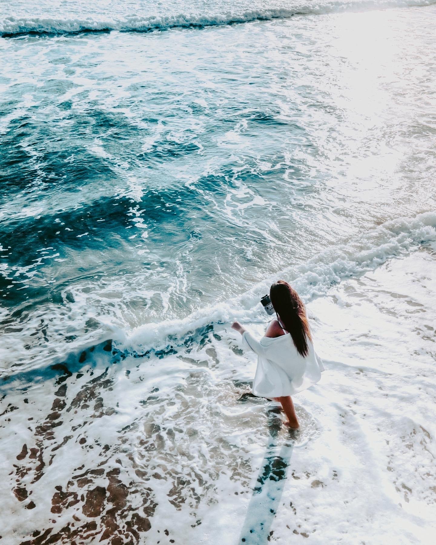 girl holding drone remote as she walks into the ocean waves