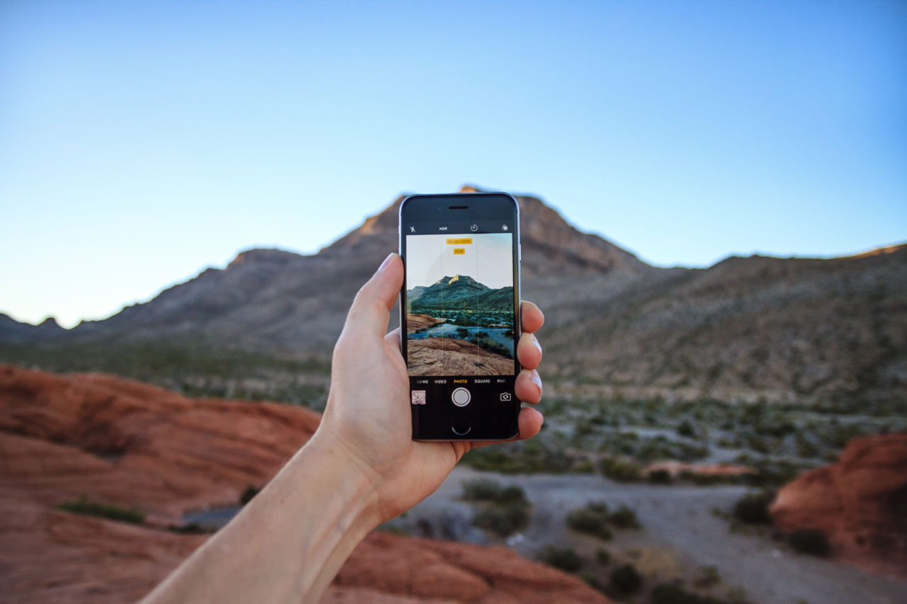 Person holding an iPhone while taking photo of a mountain scene.